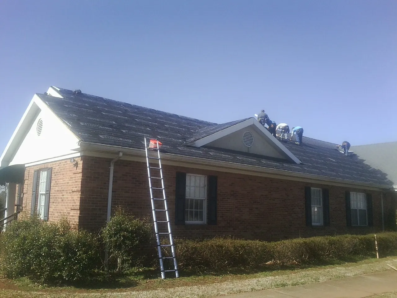 Crew tearing shingles off a brick ranch roof with a ladder set — Emergency Roof Repair work by our crew in Fairless Hills