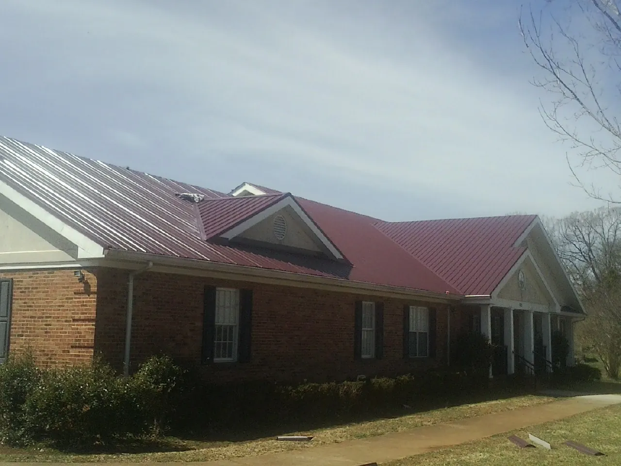 Red metal roof with gabled entries on a long brick building, from a Hail Damage Roof Repair job in Fairless Hills