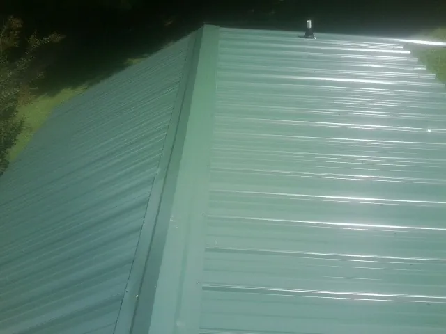 New green metal panels meeting at the ridge of a roof — Flat Roof Repair work by our crew in Fairless Hills