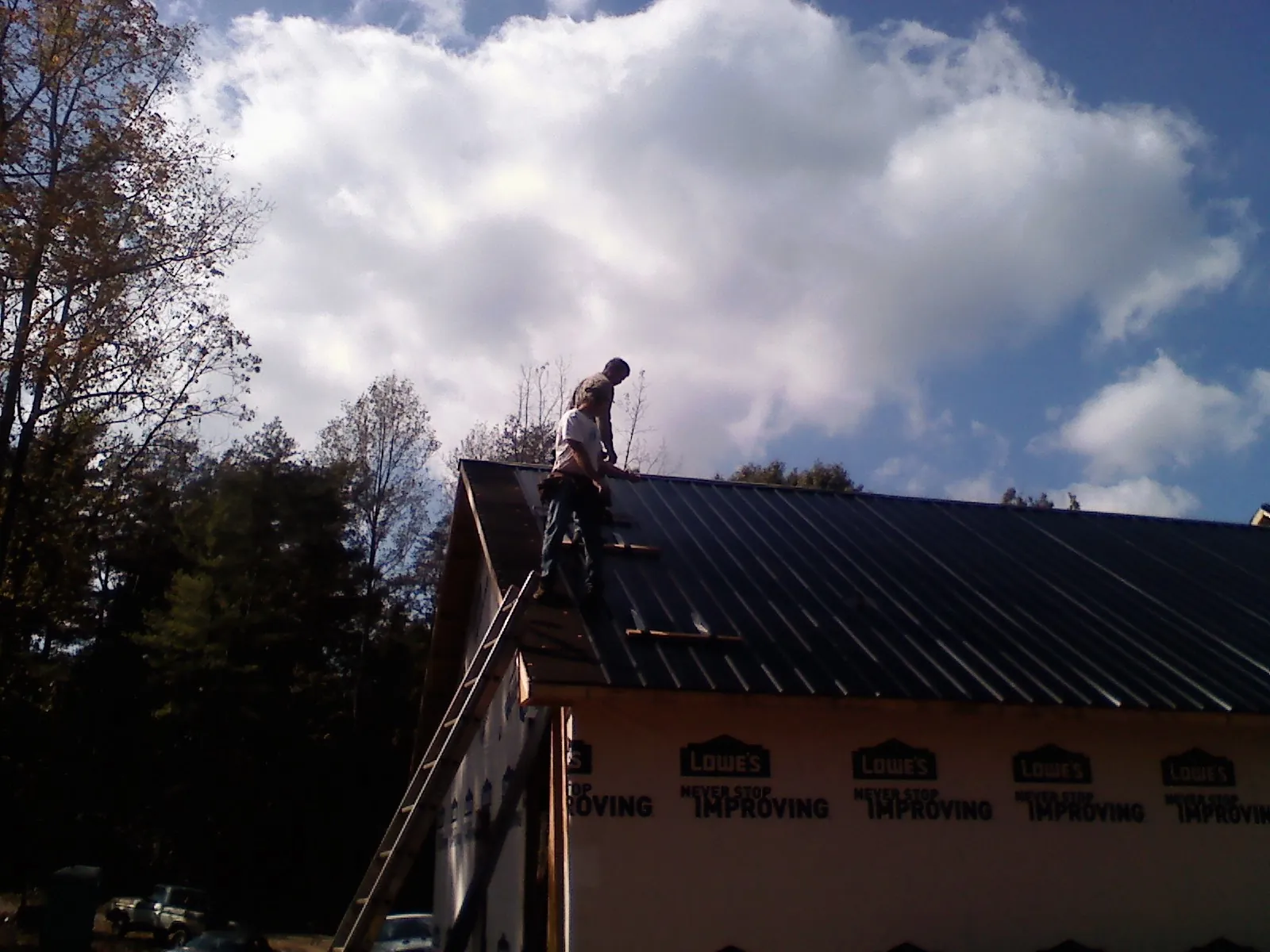 Roofer fastening dark metal panels high against a cloudy sky, from a Roof Inspection job in Fairless Hills