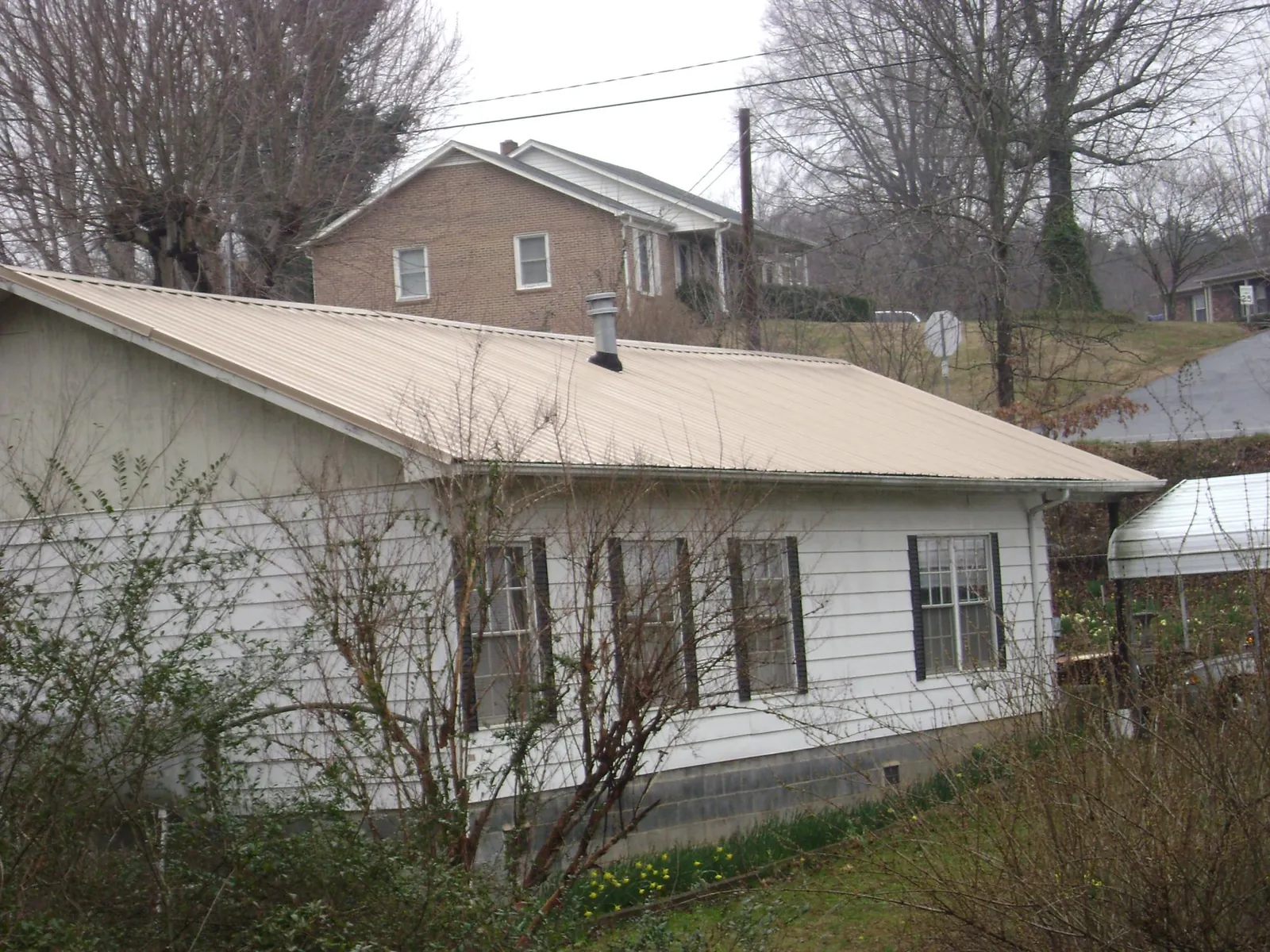 Tan metal roof on a white sided house set into a hillside — Commercial Roofing by Roofing Brothers in Fairless Hills